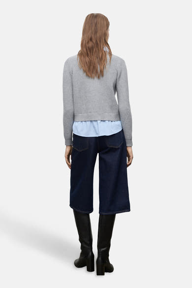 Cardigan gris de MANGO, porté sur une chemise rayée bleu clair, avec un pantalon large en denim et des bottes noires.
