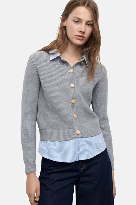 Grijze geribbelde gebreide cardigan van MANGO, gedragen over een blauw gestreept overhemd en een donkere spijkerbroek.