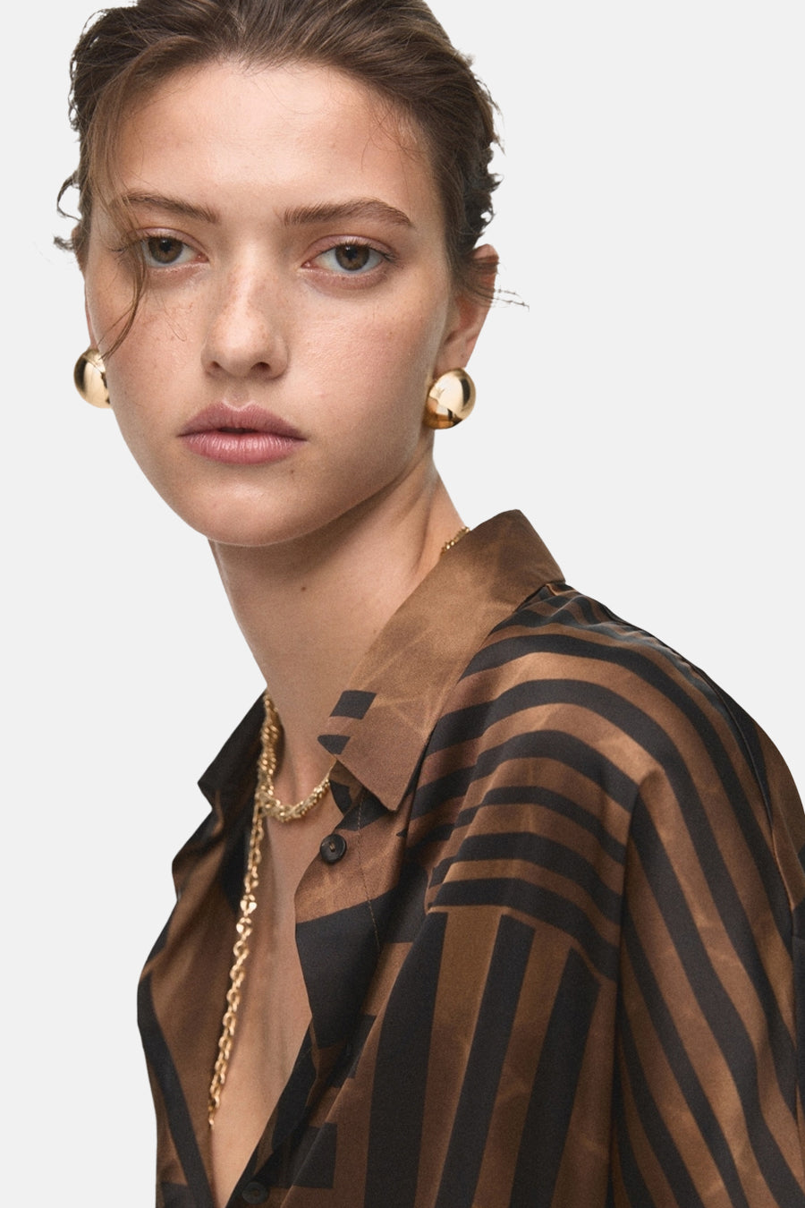 Bruin en zwart gestreept overhemd met lange mouwen van MANGO, gedragen met gouden oorbellen en ketting.