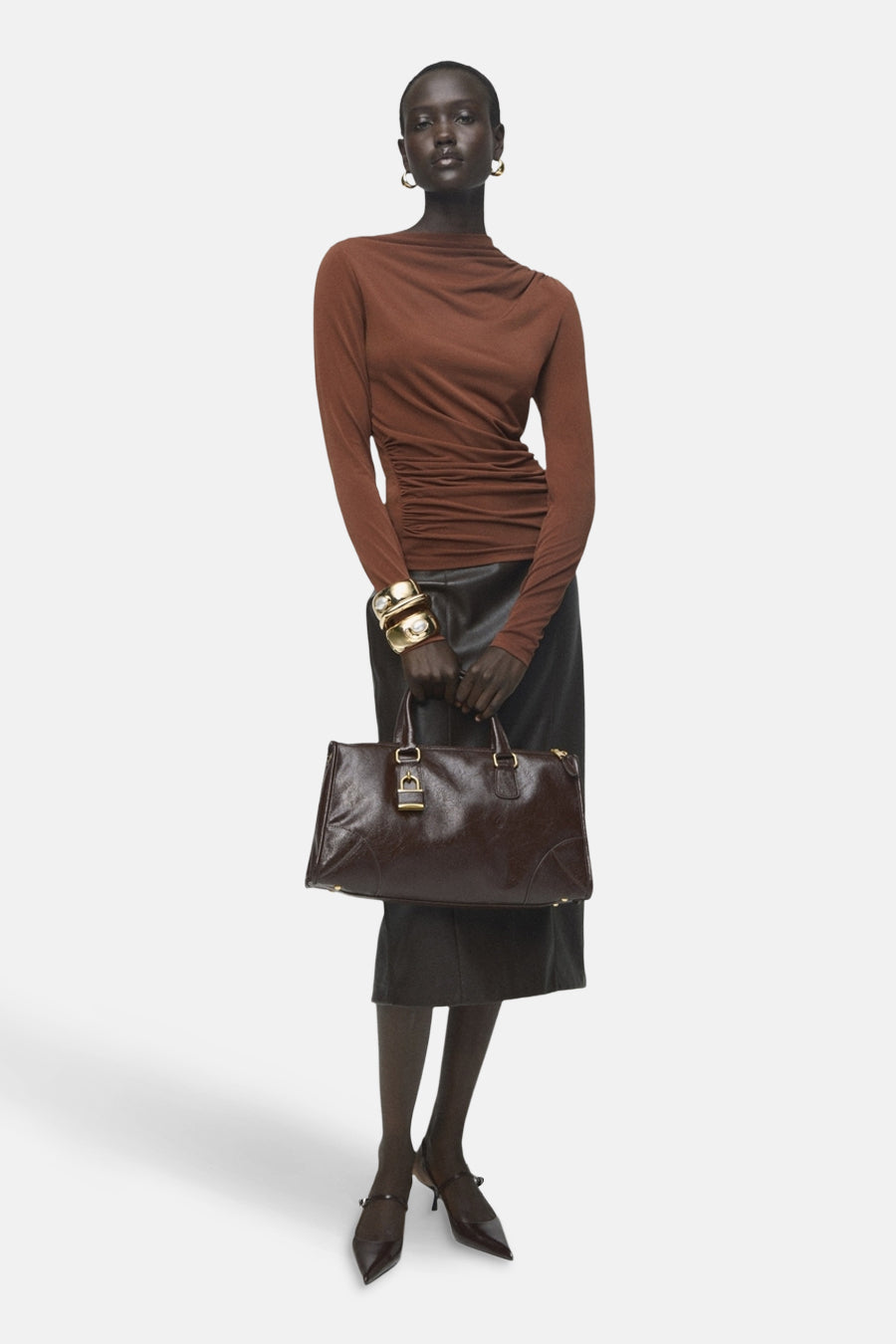 T-shirt à manches longues brun de MANGO, porté avec une jupe noire et un sac à main marron.