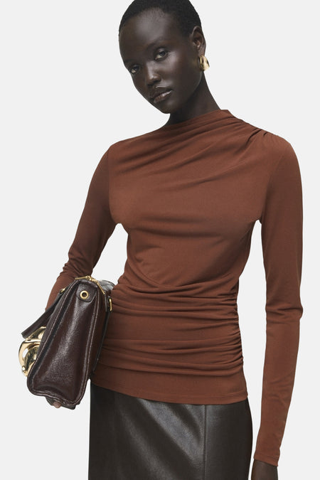 Bruin T-shirt met lange mouwen van MANGO met een gedrapeerd detail op de schouder, gedragen met een leren rok en een handtas.