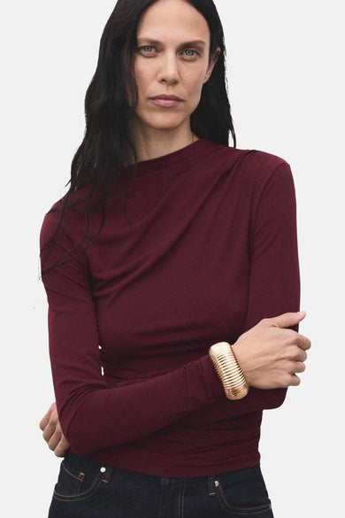 T-shirt à manches longues bordeaux de MANGO, porté avec un jean et un bracelet doré.
