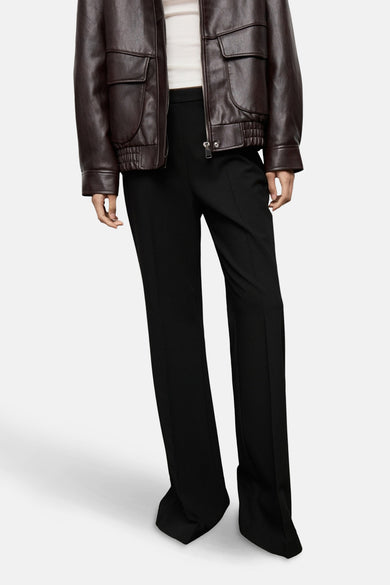 Pantalon noir de MANGO, coupe droite, porté avec un blouson en cuir marron et un haut crème.