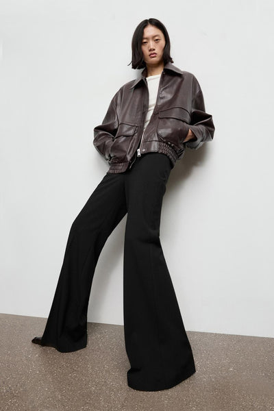 Pantalon noir de MANGO, ample et évasé, porté avec une veste en cuir marron.
