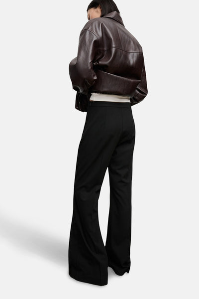 Pantalon noir de MANGO, coupe évasée, avec un haut blanc et une veste marron en cuir.