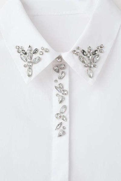 Chemise blanche à manches longues de MANGO, ornée de strass décoratifs sur le col et la patte de boutonnage.

