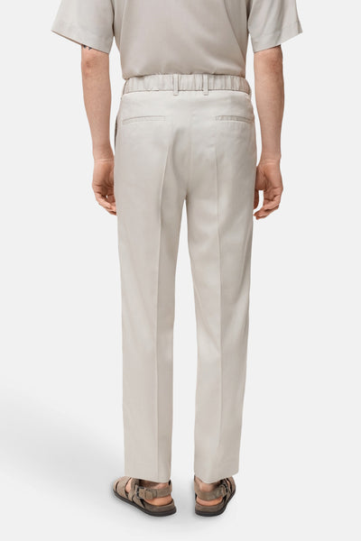 Ecru broek van MANGO, met elastische taille, van achteren gezien, gedragen met leren sandalen.