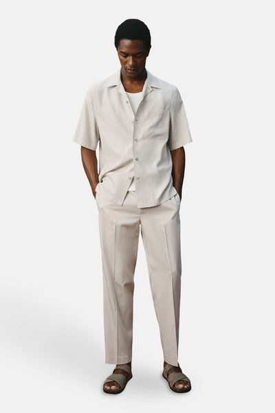 Pantalon écru de MANGO, porté avec une chemise et des sandales assorties.