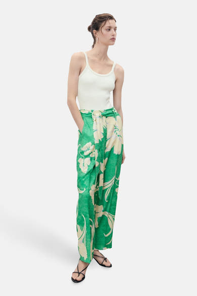 Groene broek met bloemenprint van MANGO, gedragen met een witte tanktop en zwarte sandalen.