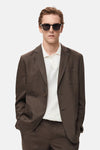 Blazer brun de MANGO, porté par un homme avec un polo blanc et des lunettes de soleil.