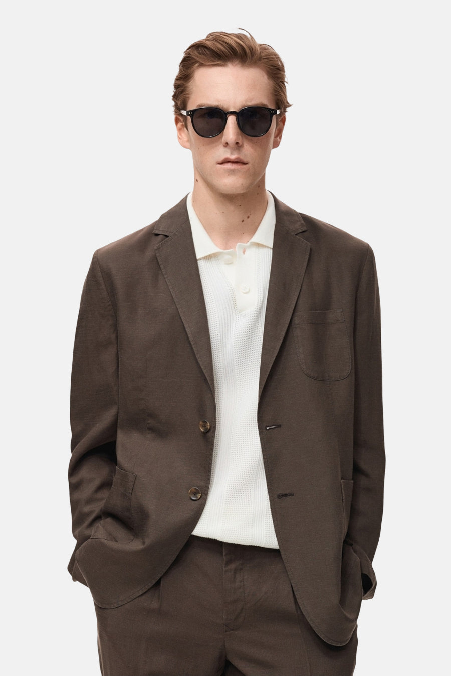 Blazer brun de MANGO, porté par un homme avec un polo blanc et des lunettes de soleil.