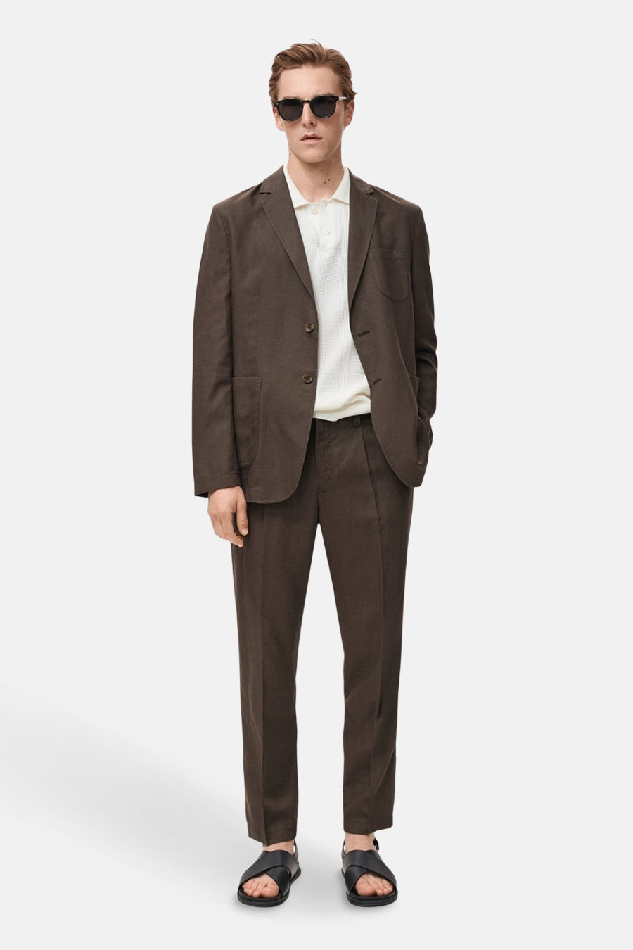 Blazer brun de MANGO, porté avec un polo blanc et des sandales en cuir noir.
