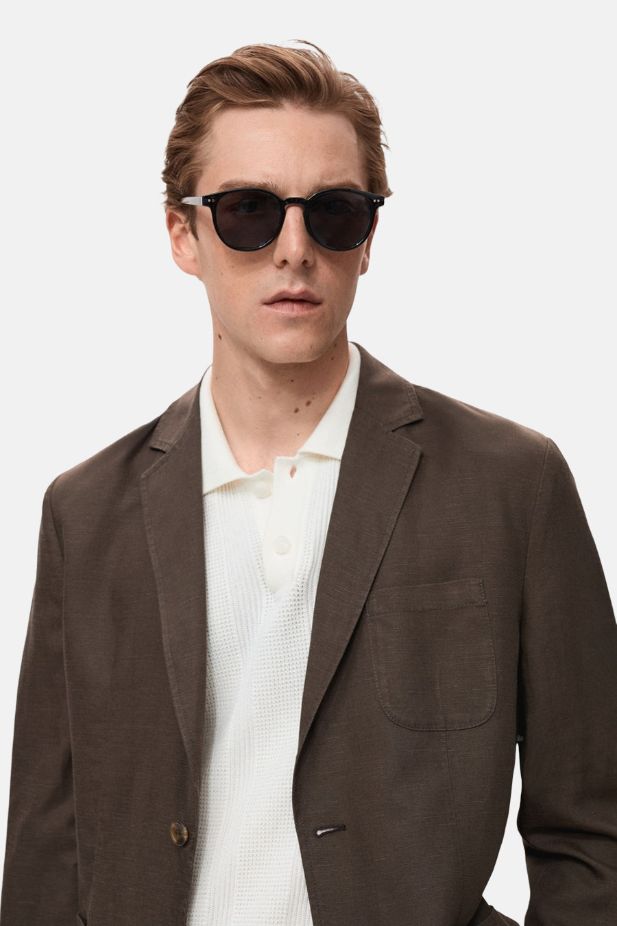 Blazer brun de MANGO, porté sur un polo blanc texturé, avec lunettes de soleil rondes.