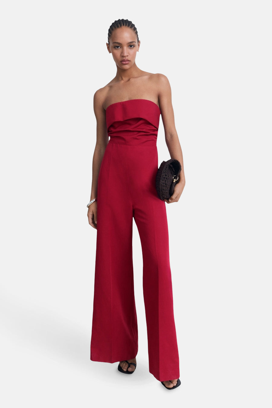 Combinaison rouge par MANGO avec coupe tube et jambes larges, portée avec une pochette foncée et des sandales.
