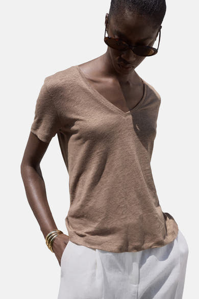 Bruin T-shirt met korte mouwen, van MANGO, gedragen met een witte broek en gouden armbanden.