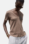 Bruin T-shirt met korte mouwen, van MANGO, gedragen met een witte broek en gouden armbanden.
