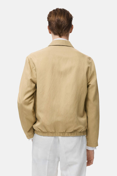 Korte beige jas van MANGO, van achteren gezien, met elastische zoom en klassieke kraag gedragen met een witte broek.