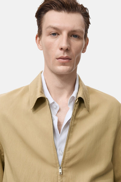 Veste courte beige de MANGO, portée sur une chemise blanche, avec une fermeture éclair visible.