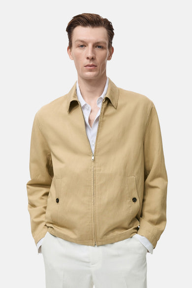 Korte beige jas van MANGO, met ritssluiting en zakken met knopen, gedragen over een wit overhemd en een witte broek.