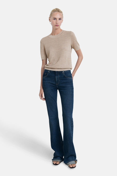 Pull beige à col rond de MANGO, porté avec un jean évasé bleu et des sandales.
