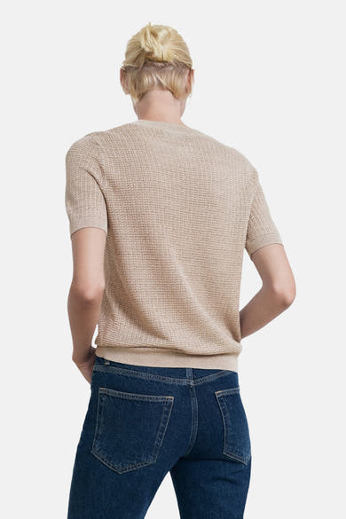 Pull à col rond beige de MANGO, à maille texturée, porté avec un jean bleu foncé, vue de dos.

