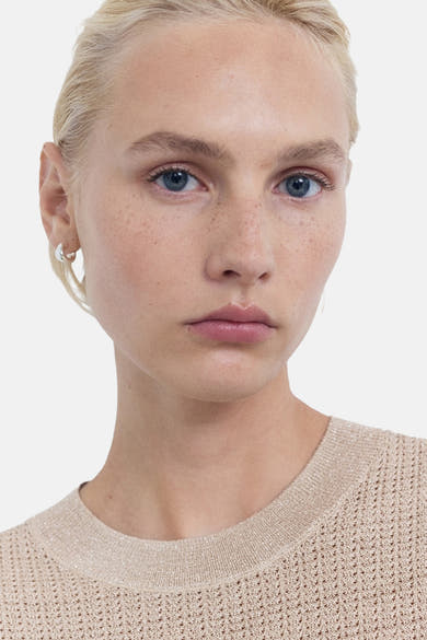 Beige ronde hals trui van MANGO, in ajour gebreid, gedragen met zilveren oorbellen.