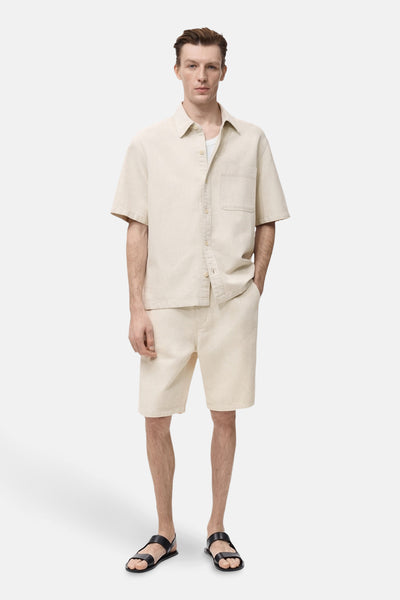 Ecru spijkerblouse van MANGO, open gedragen over een wit T-shirt met een bijpassende korte broek en zwarte sandalen.