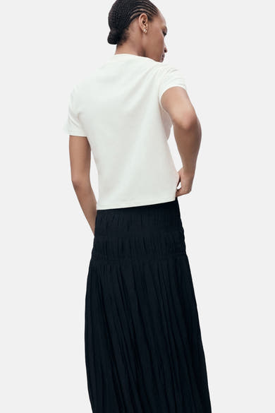 Ecru T-shirt met korte mouwen van MANGO, gedragen met een zwarte geplooide rok.