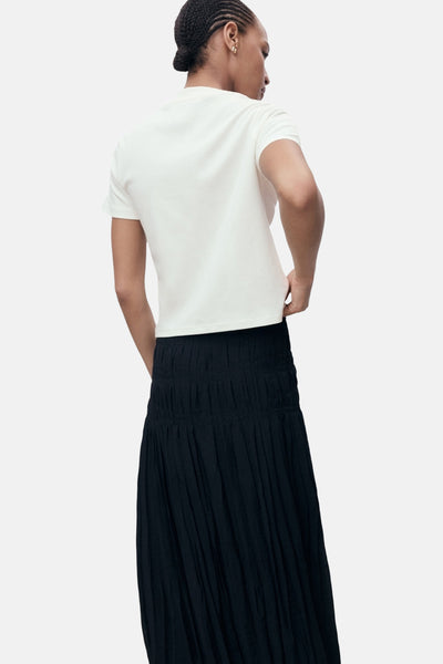 Ecru T-shirt met korte mouwen van MANGO, gedragen met een zwarte geplooide rok.