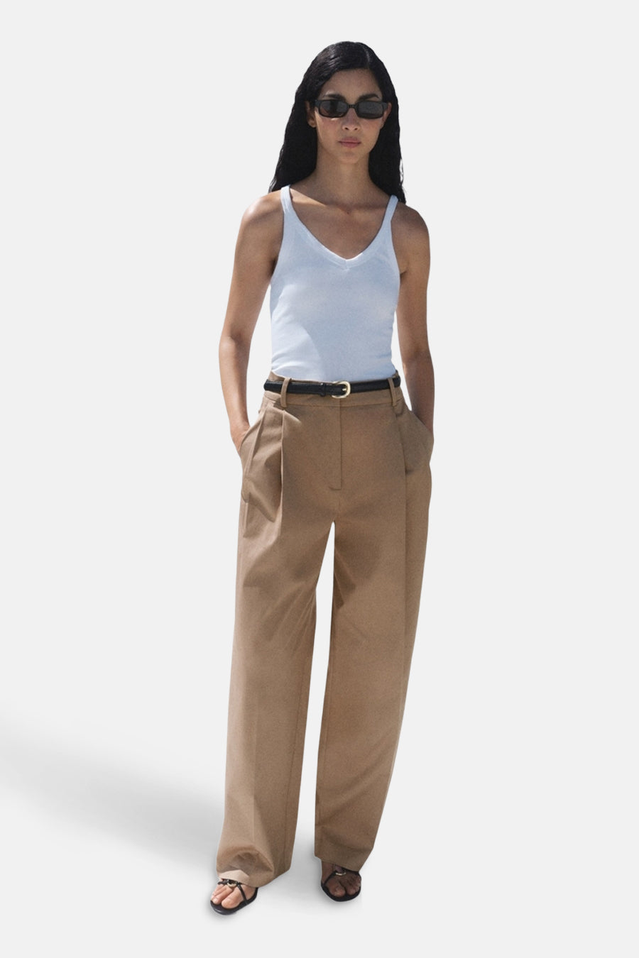 Pantalon beige de MANGO, ample avec ceinture noire et sandales, porté avec un débardeur blanc.
