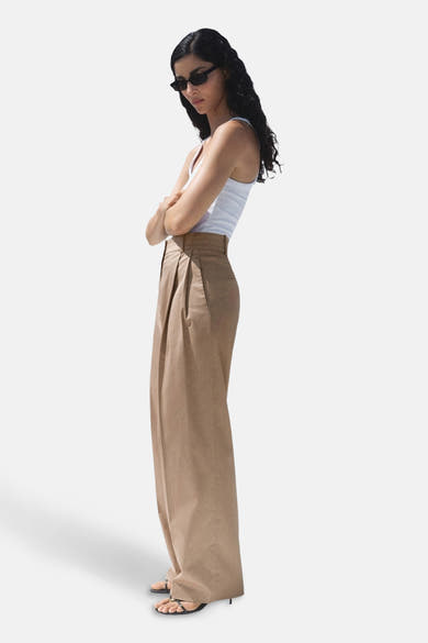Pantalon beige de MANGO, coupe ample avec plis à la taille, porté avec un débardeur blanc.