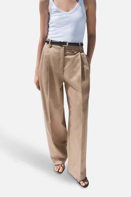 Beige broek van MANGO, wijd met plooien, gedragen met een zwarte riem en sandalen.