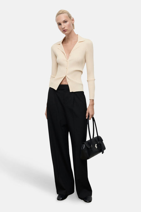 Gele MANGO-cardigan in ribgebreide stof, gedragen met een wijde zwarte broek en een zwarte leren handtas.
