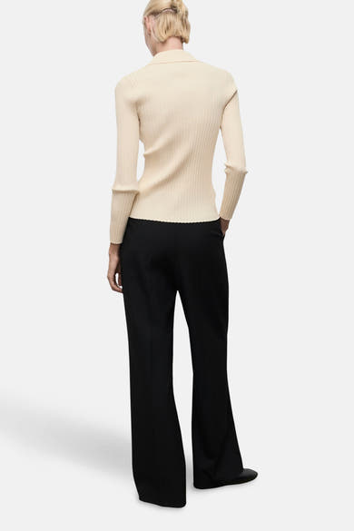 Gele geribde cardigan van MANGO, gedragen met een zwarte uitlopende broek, achtergezicht.