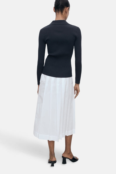 Blauwe geribbelde cardigan van MANGO, gedragen met een witte geplooide rok en zwarte muiltjes, van achteren gezien.