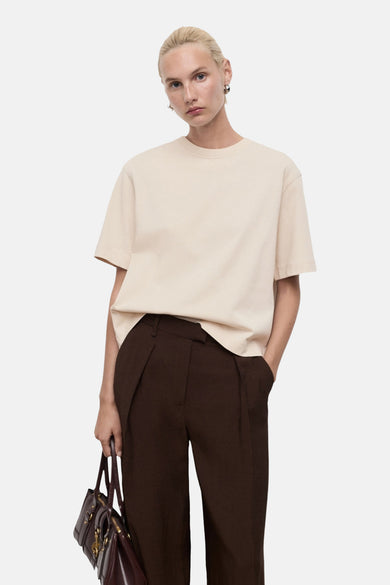 Beige T-shirt met korte mouwen van MANGO, gedragen met een bruine broek en een donkere handtas.