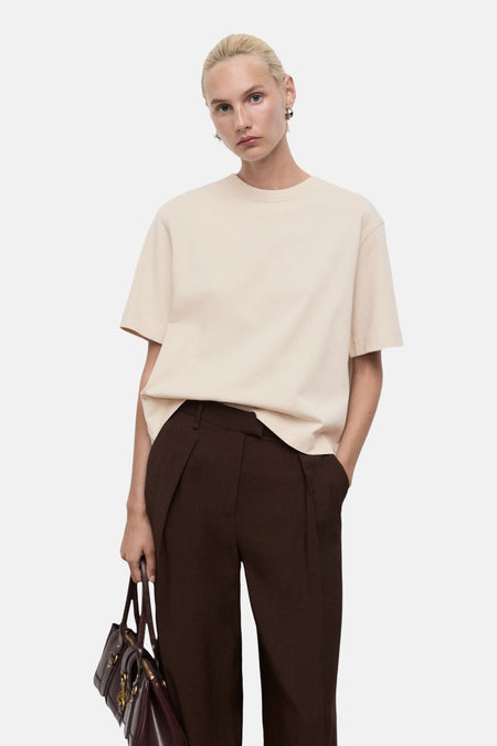 Beige T-shirt met korte mouwen van MANGO, gedragen met een bruine broek en een donkere handtas.