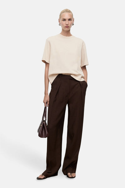 Beige T-shirt met korte mouwen van MANGO, gedragen met een bruine plooibroek en een bordeauxrode handtas.