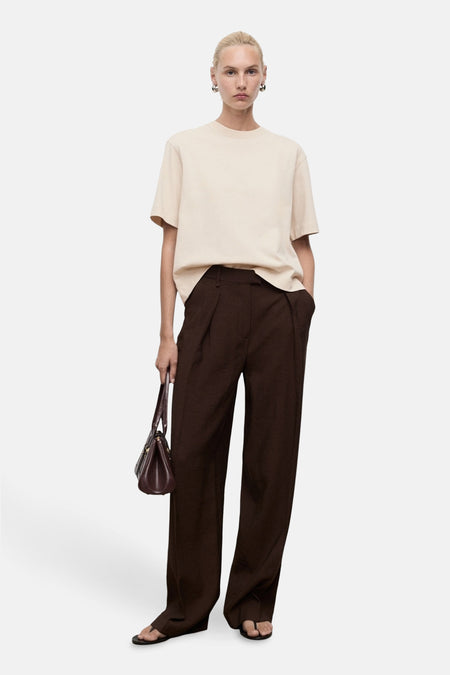 Beige T-shirt met korte mouwen van MANGO, gedragen met een bruine plooibroek en een bordeauxrode handtas.