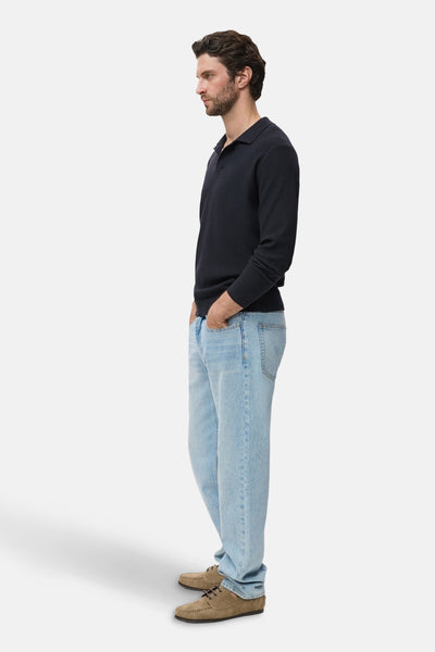 Pull à col rond bleu de MANGO, porté avec un jean clair et des chaussures en daim marron, en vue latérale.
