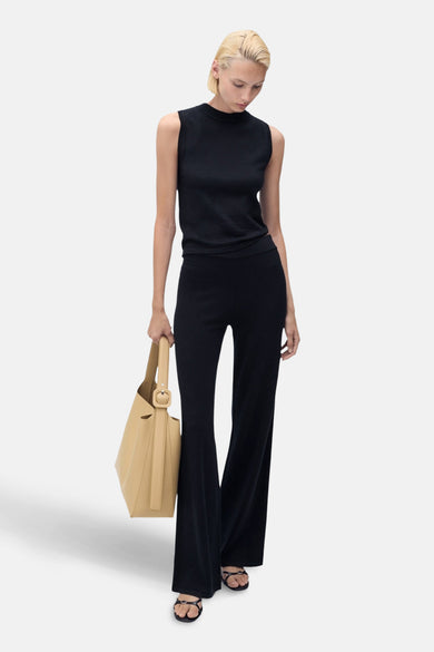 Pantalon bleu de MANGO, ample et évasé, porté avec un haut noir sans manches et des sandales à brides.