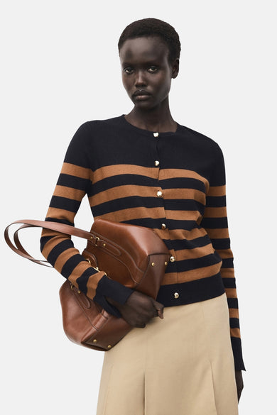 Cardigan rayé noir et marron de MANGO, porté avec un pantalon beige et un sac à main en cuir marron.
