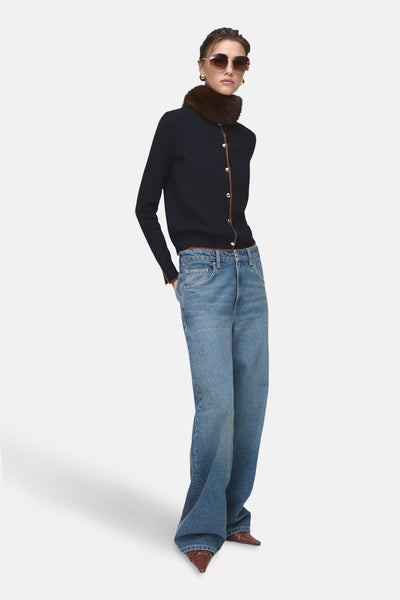 Cardigan bleu foncé de MANGO, avec bordure marron et boutons dorés, porté avec un jean bleu et des chaussures marron.
