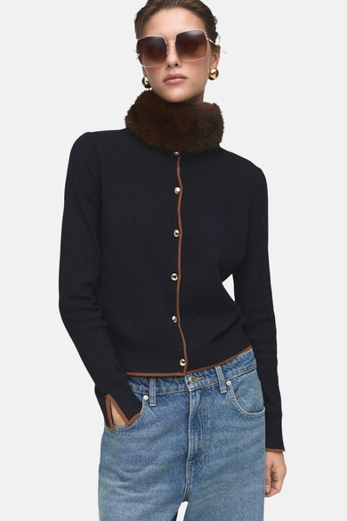Cardigan bleu foncé de MANGO avec une garniture marron, porté avec un col en fourrure et un jean décontracté.
