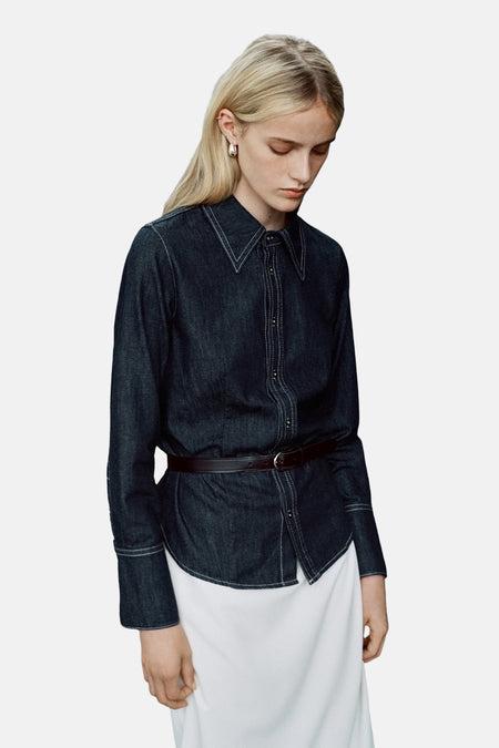 Donkerblauwe spijkerblouse met lange mouwen van MANGO, met bruine riem en witte stikseldetails.