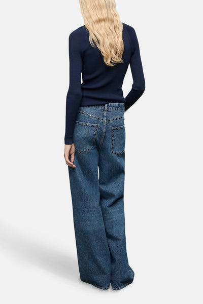 Wijde jeans van donkerblauw denim van MANGO, versierd met decoratieve studs en gedragen met een marineblauwe trui.
