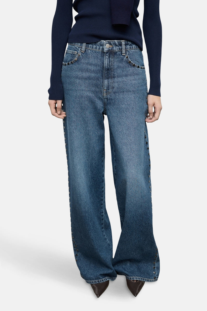 Wijde spijkerbroek in donkerblauw denim van MANGO, met klinknageldetails aan de zijkanten en gedragen met een marineblauwe trui.