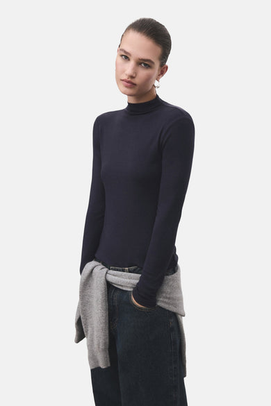 T-shirt bleu à manches longues de MANGO, porté avec un pull gris noué autour de la taille.
