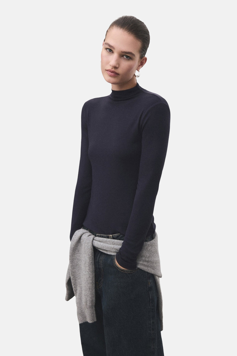 T-shirt bleu à manches longues de MANGO, porté avec un pull gris noué autour de la taille.
