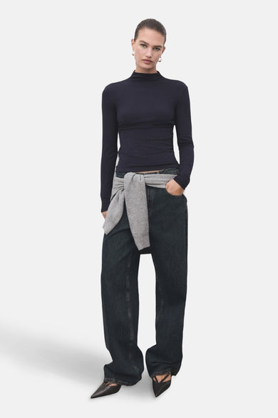 T-shirt bleu à manches longues de MANGO, porté avec un pull gris noué à la taille et un jean ample.
